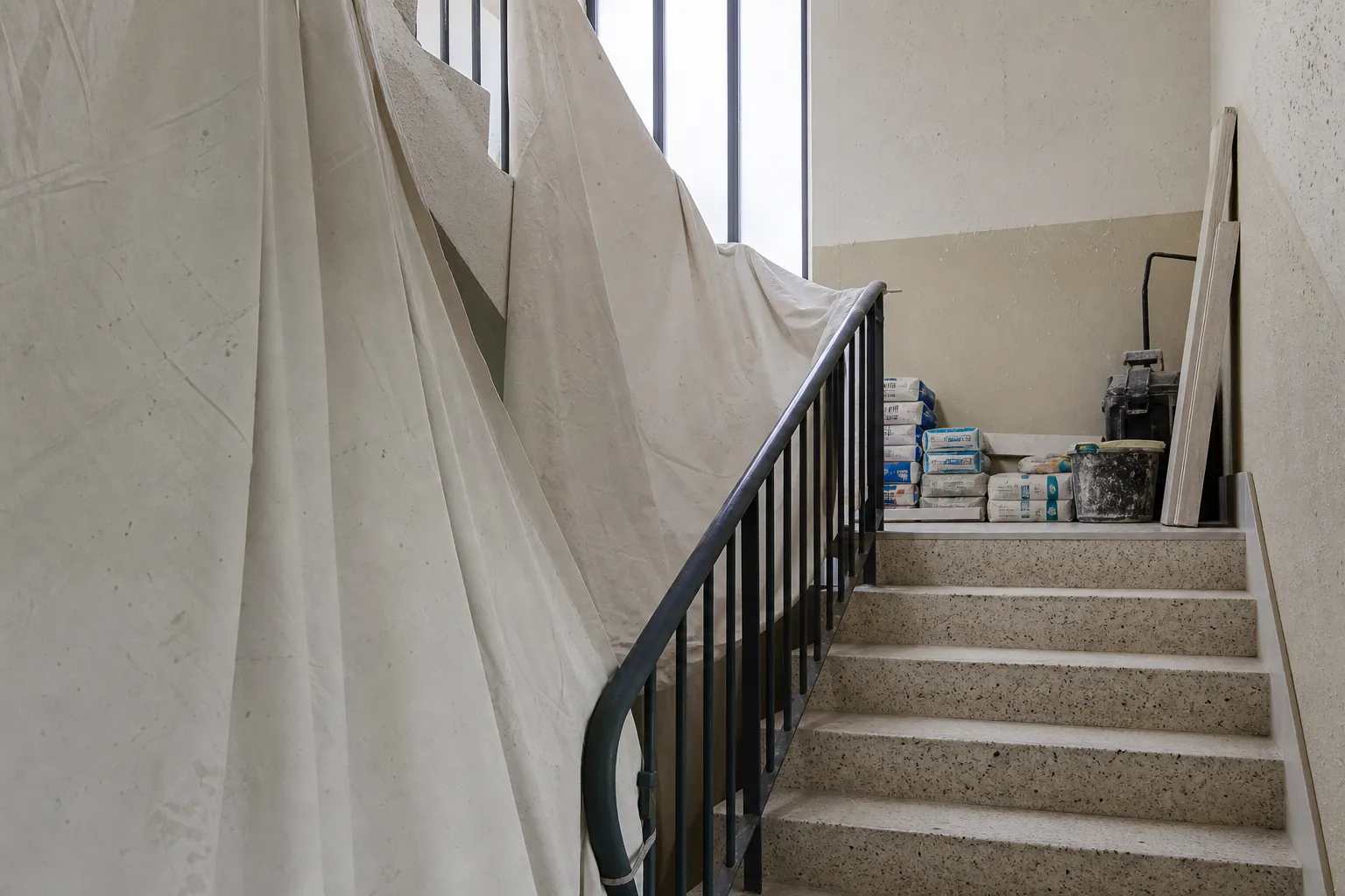 Cage d’escalier d’immeuble d’après-guerre, parties communes protégées par des bâches et matériaux stockés