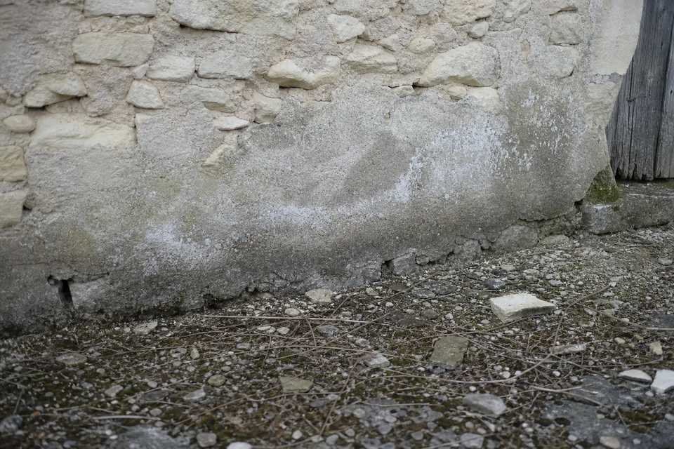 Pied de mur ancien en moellon : enduit ciment dégradé et remontée d’humidité visible