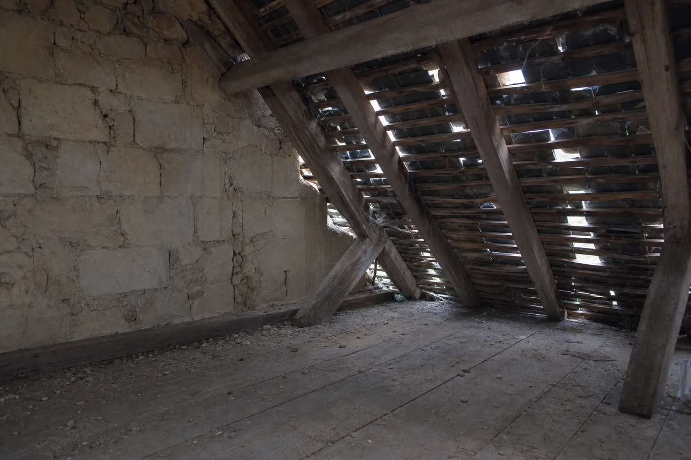 Comble non isolé vu de l’intérieur : plancher, charpente ancienne et jour visible entre les ardoises